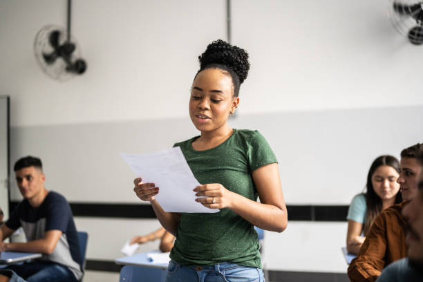 Photographie d'une étudiante debout dans une classe en train de réciter son oral.